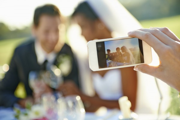 Shot of a wedding guest taking a photo of the bride and groom will a cellphone