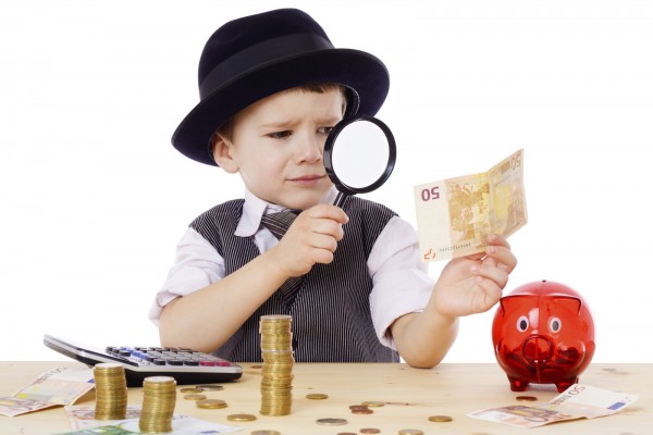 Little businessman checks the money with magnifying glass, isolated on white